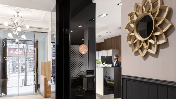 Rebedor modern d'hotel amb taulell de recepció, un mirall gran i un senyal que indica un comerç de menjar proper.