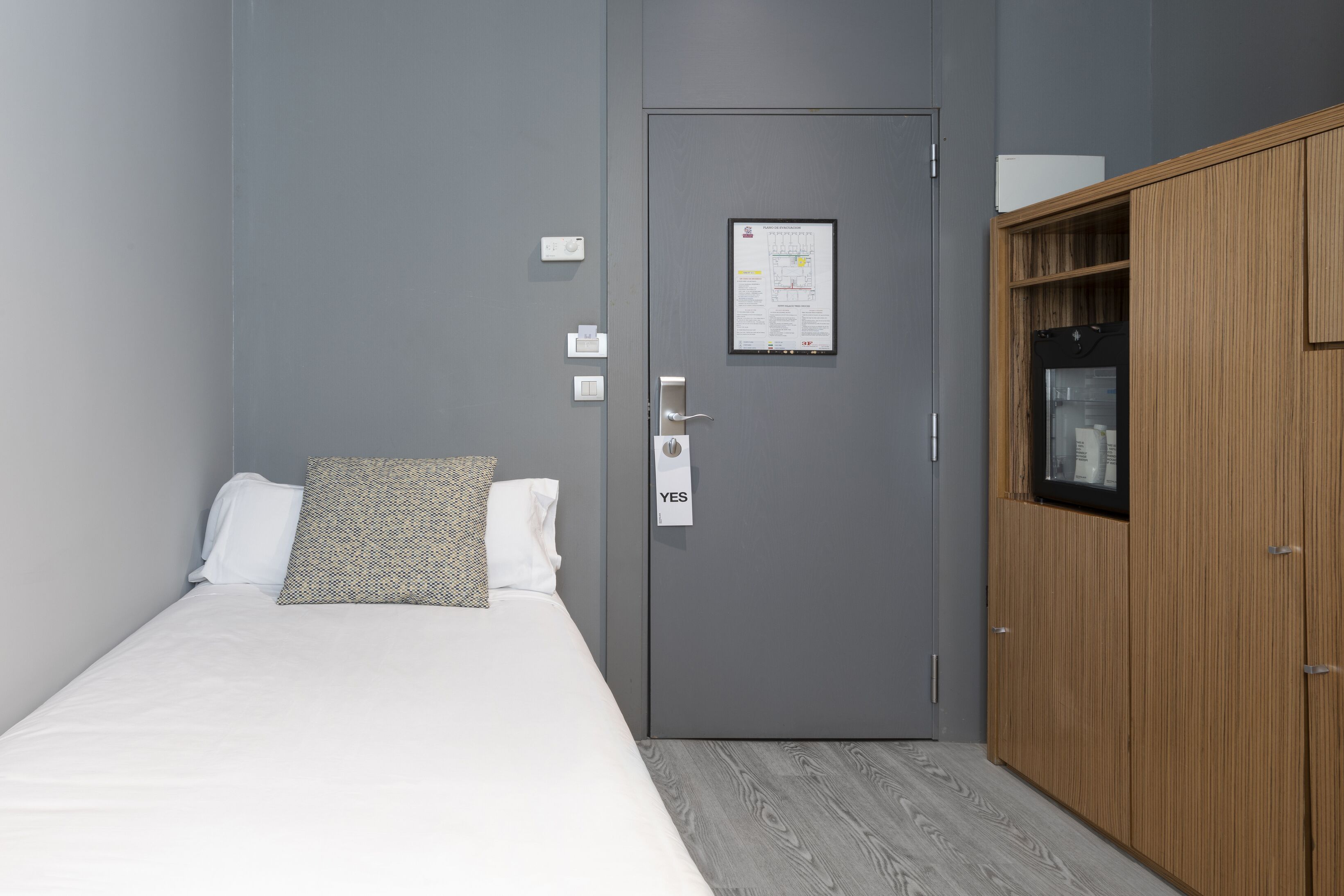 Un dormitorio con cama, una puerta gris con un letrero que dice 'YES', un armario de madera y una ventana pequeña.