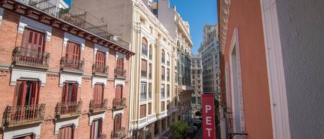 Una calle estrecha bordeada de edificios de varios pisos, con balcones de barandilla de hierro forjado y contraventanas rojas.