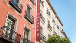 Un edifici amb façana vermella i blanca, un cridaner rètol de 'PETIT PALACE HOTELS' i balcons amb baranes de ferro.