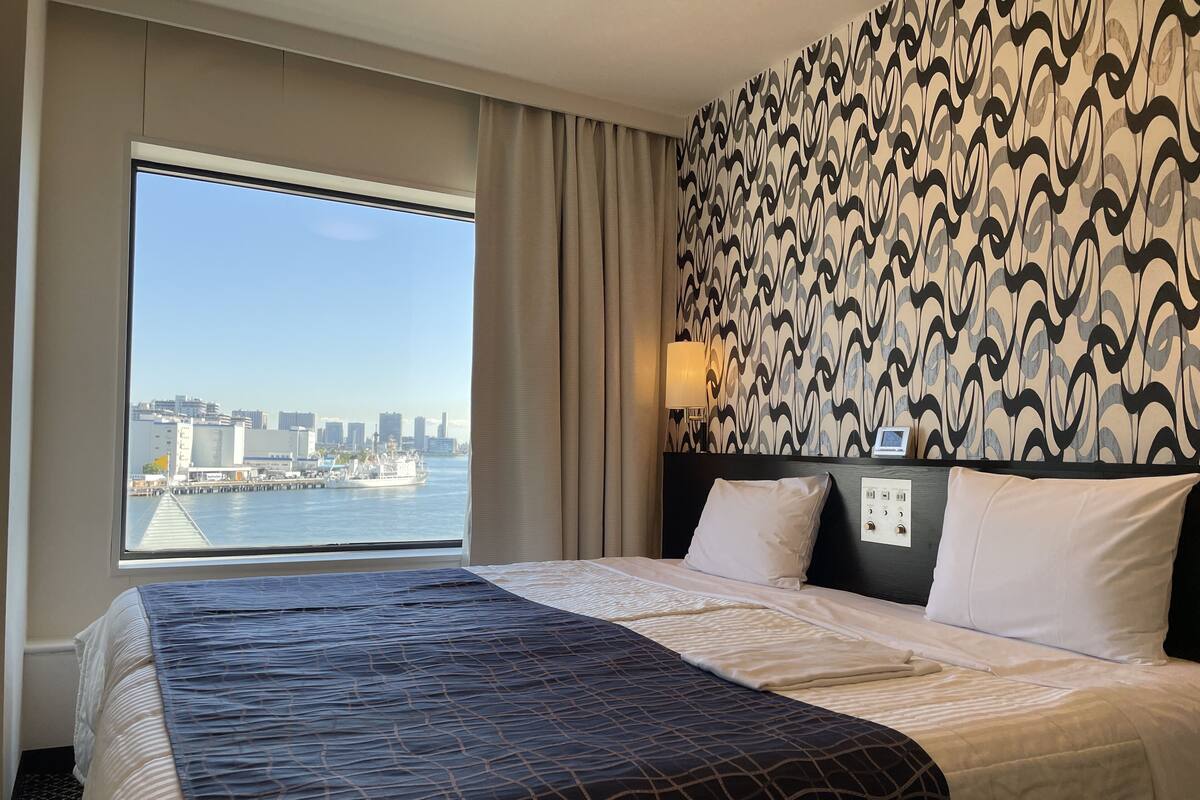 Une chambre d’hôtel avec un grand lit, une vue sur les toits de la ville et sur l’eau, et un mur décoré d’un motif.