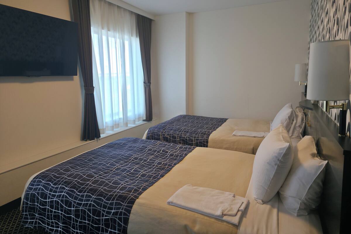 Une chambre d’hôtel avec deux lits, un téléviseur à écran plat, une fenêtre avec des rideaux et une lampe de chevet.