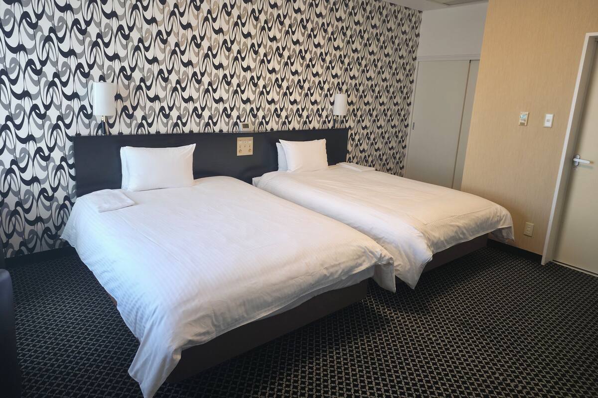 Une chambre d’hôtel avec deux lits, un papier peint à motifs, une tête de lit sombre et un sol recouvert de moquette.