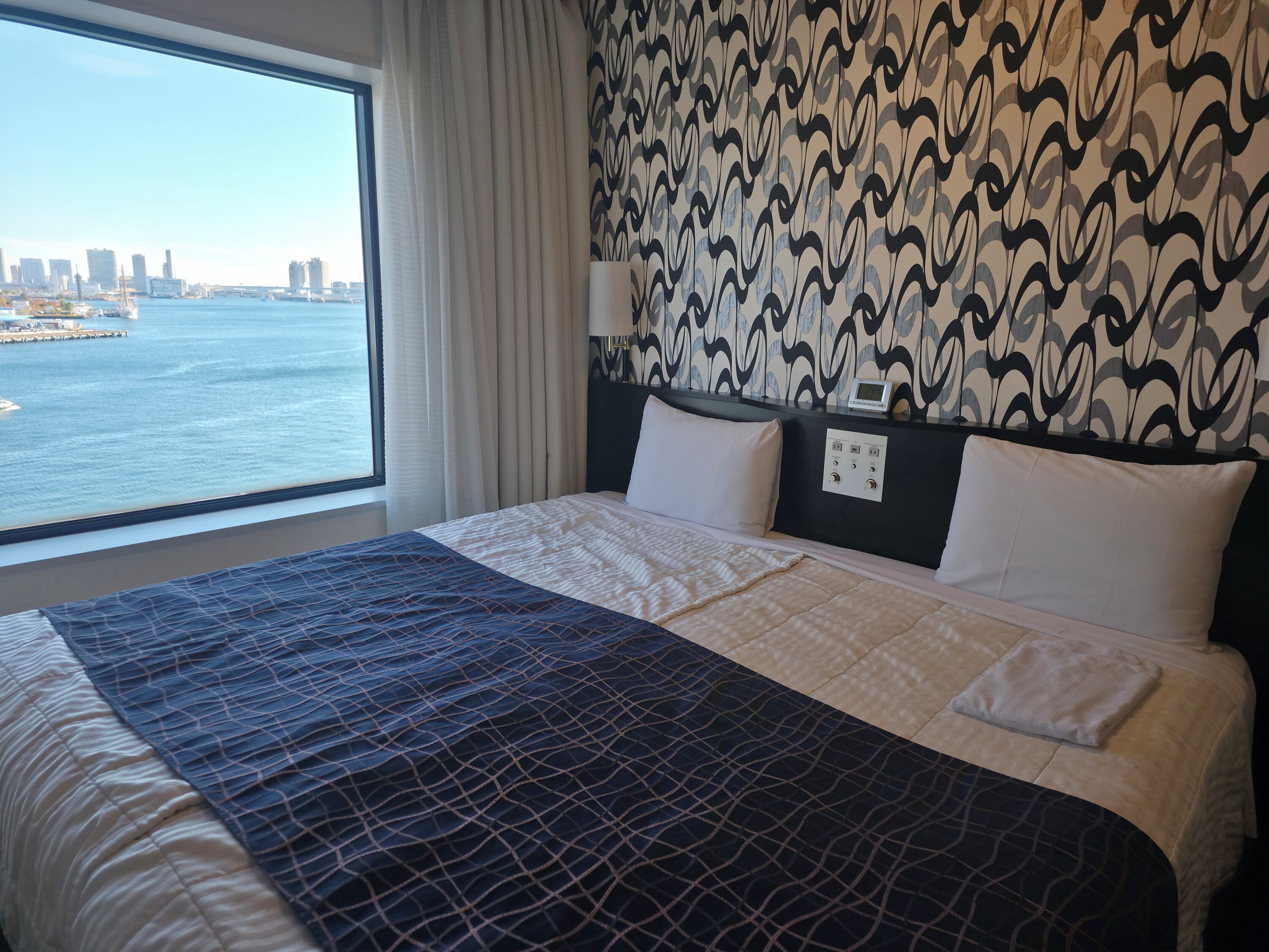 Et hotelværelse med en stor seng, udsigt til byens skyline og en stribet væg.