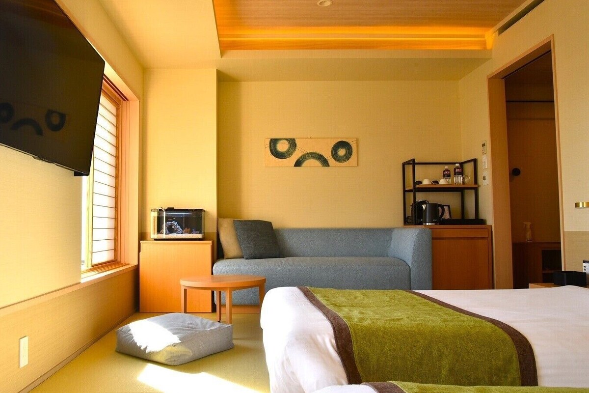 Une chambre d’hôtel avec un lit, un canapé, une petite table, un aquarium et un téléviseur fixé au mur.