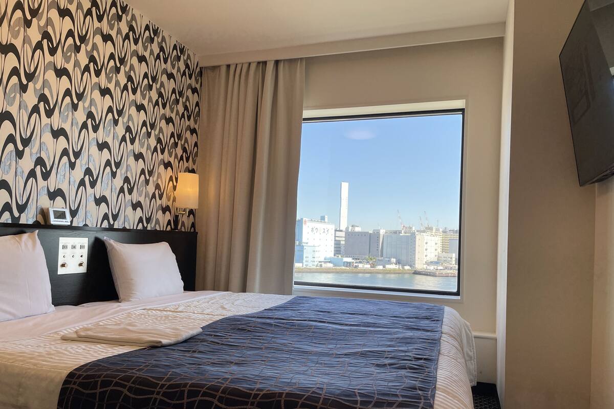 Une chambre d’hôtel avec un lit, une fenêtre donnant sur la ville, un mur décoré d’un motif et un téléviseur fixé au mur.