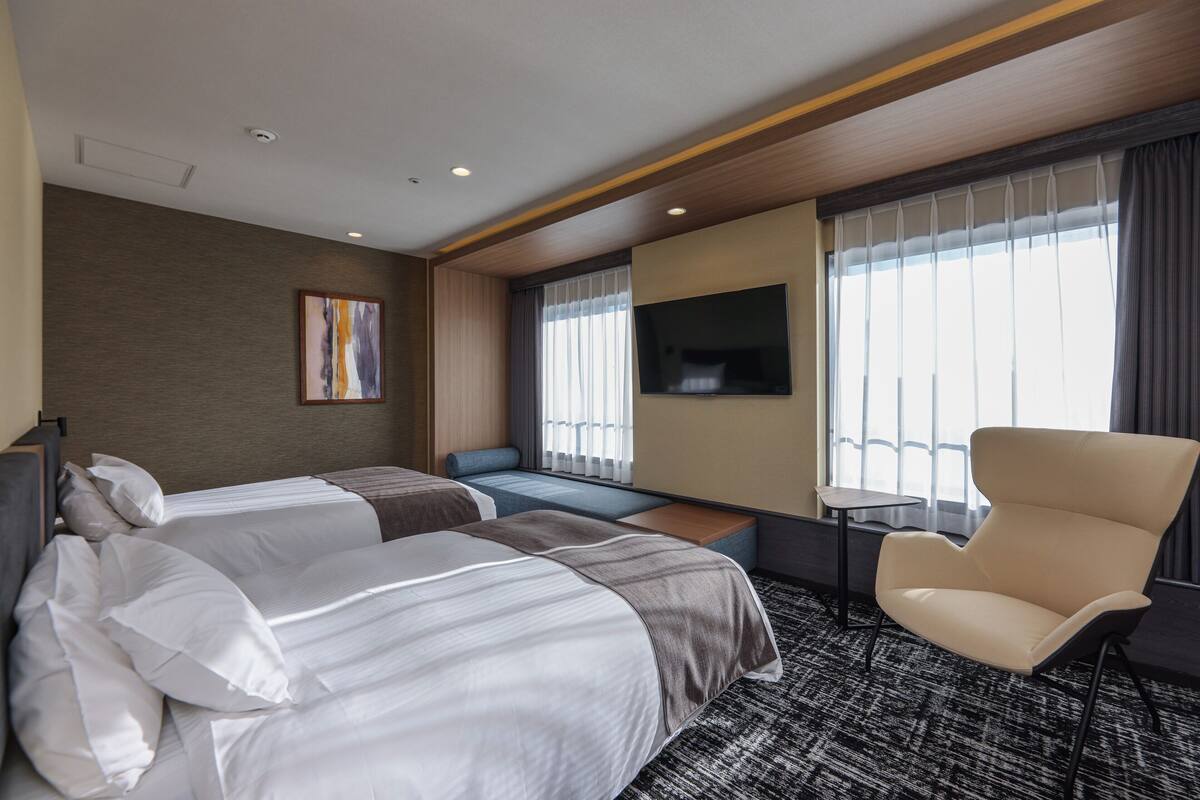 Une chambre d’hôtel avec deux lits, un canapé, une télévision et une fenêtre avec des rideaux.
