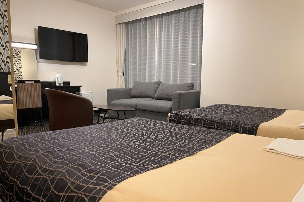 Une chambre d’hôtel avec deux lits, un canapé, un bureau, une télévision et une fenêtre avec des rideaux.
