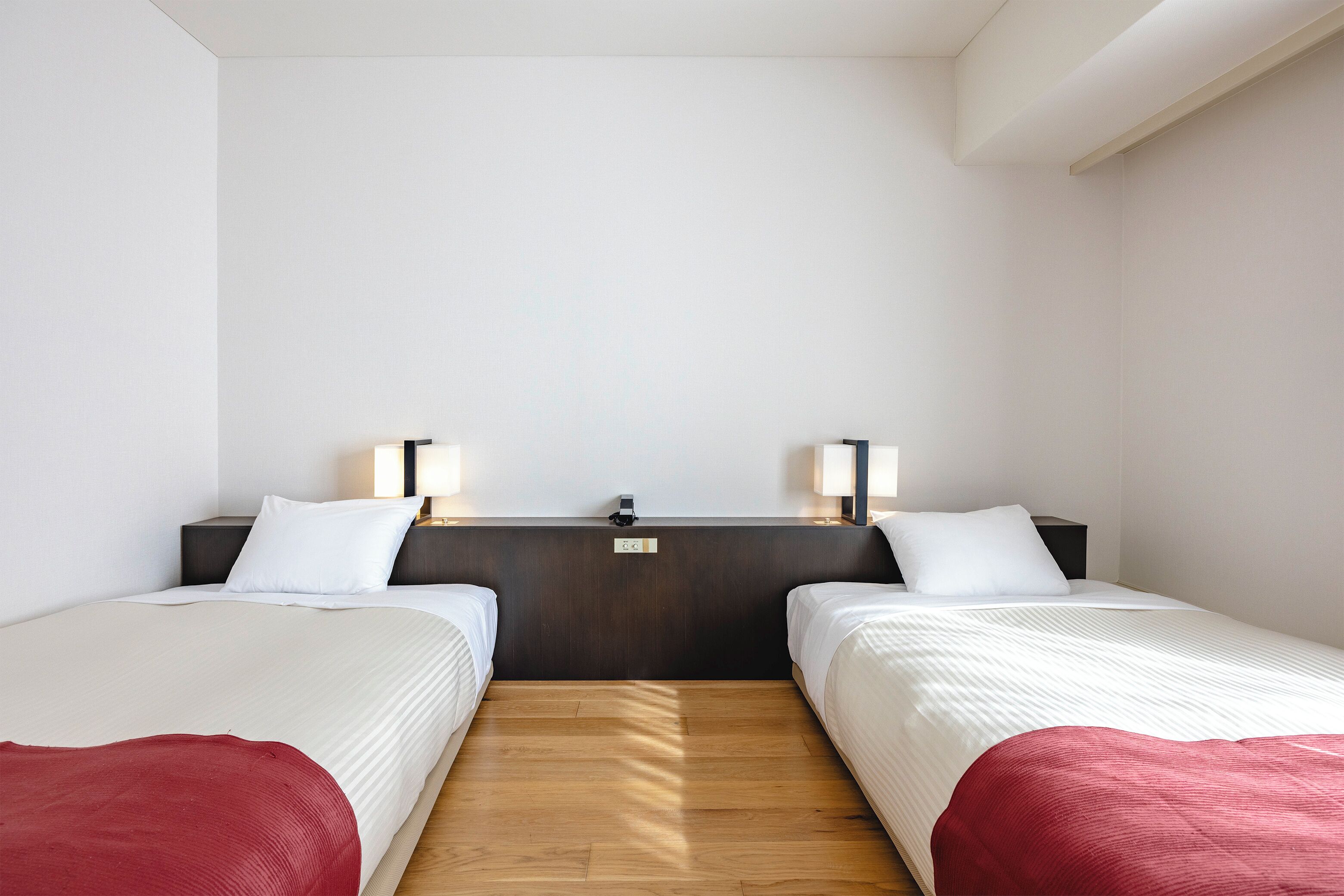 A hotel room with two single beds, a wooden floor, a dark headboard, and bedside lamps.