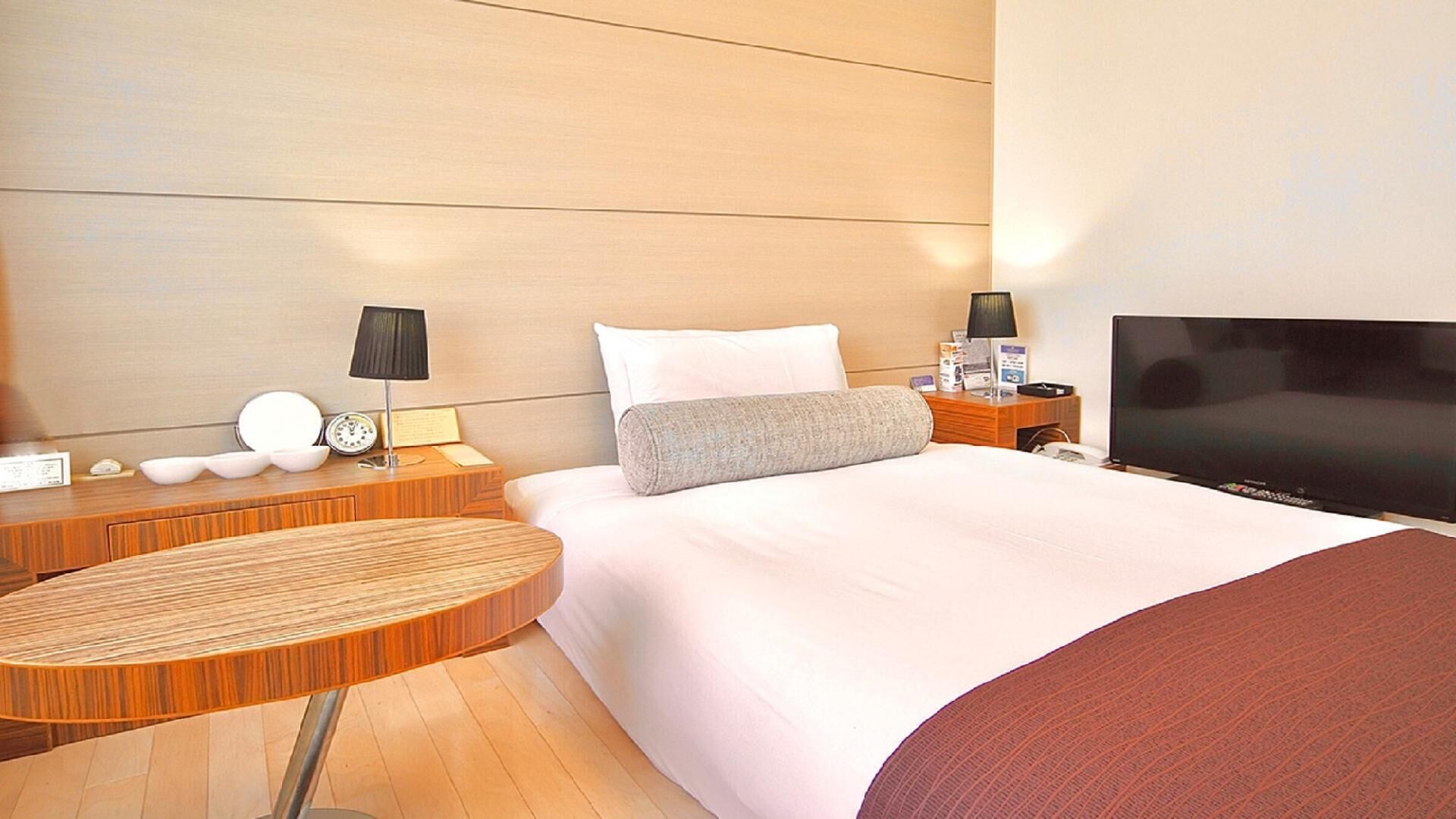 A hotel room with a bed, bedside tables, a TV, and a wooden side table.
