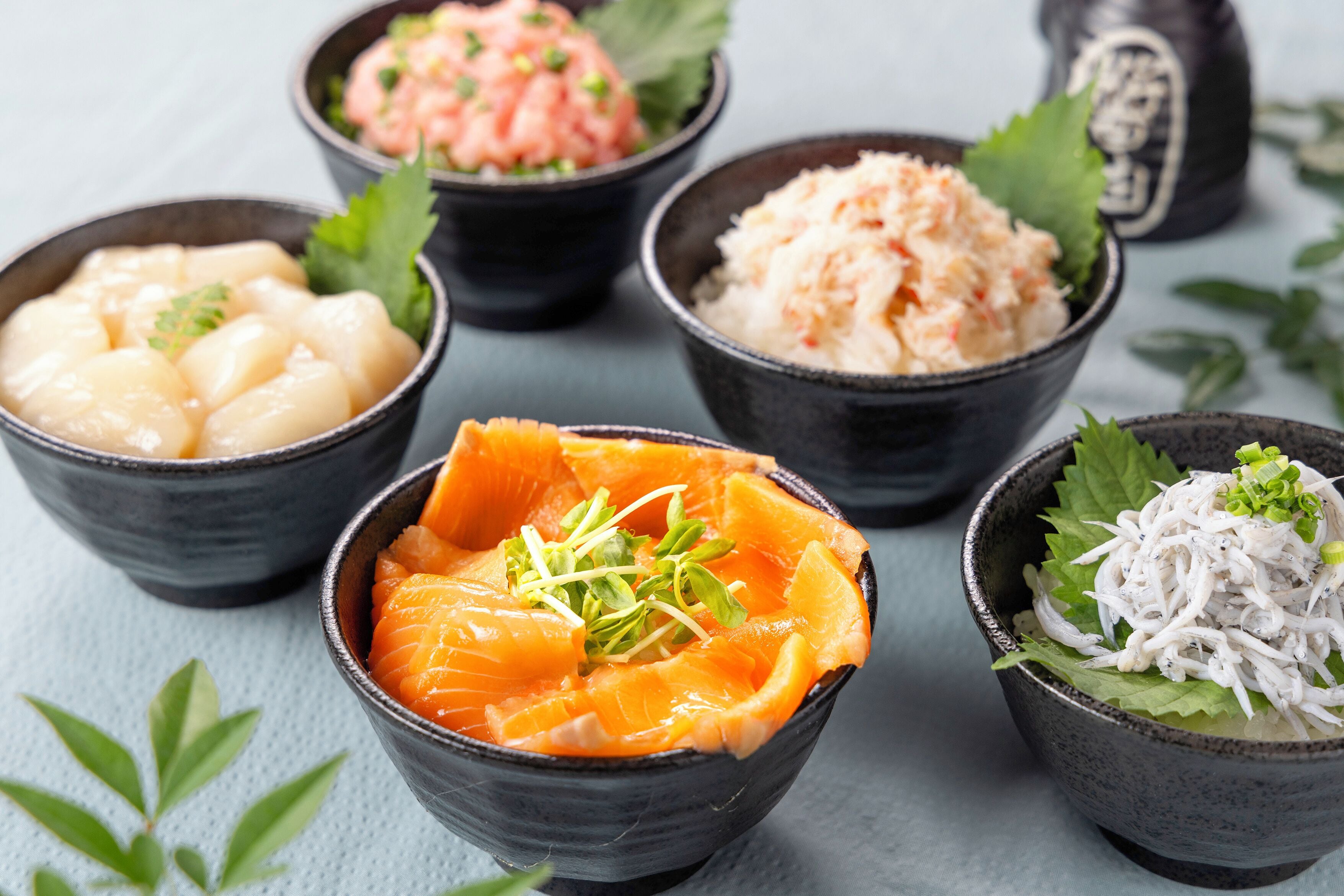 Plusieurs bols contenant différents types d’aliments, vraisemblablement des plats de la cuisine japonaise, sont disposés sur une table.