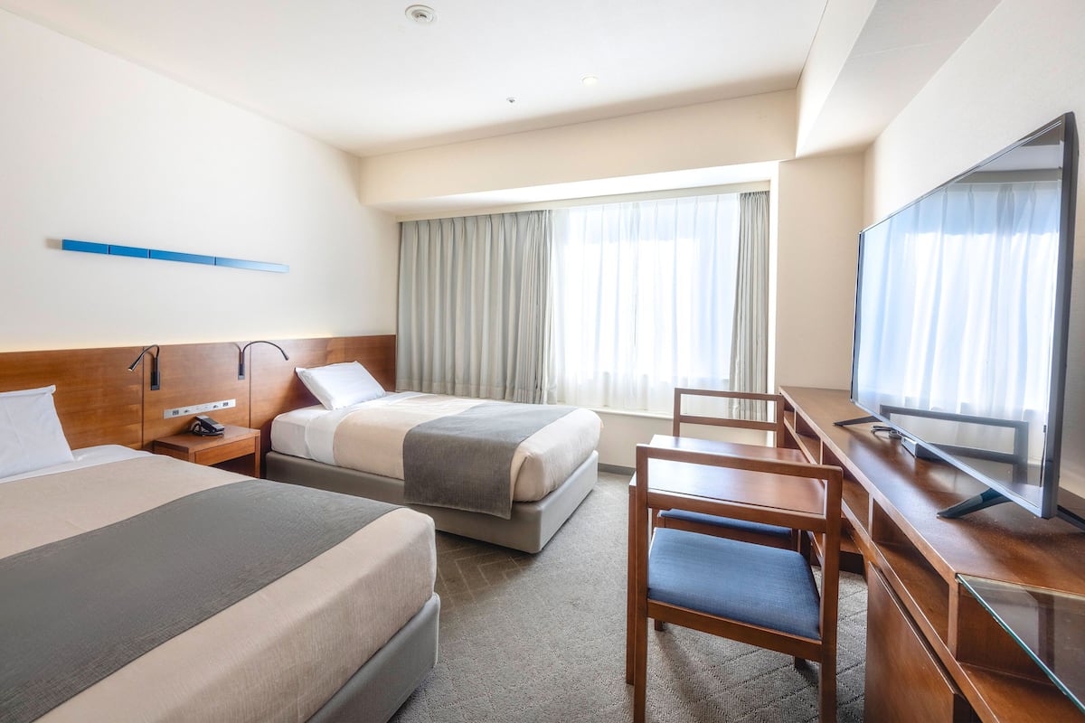 Une chambre d’hôtel avec deux lits, un bureau, une chaise, une télévision et une fenêtre avec des rideaux.