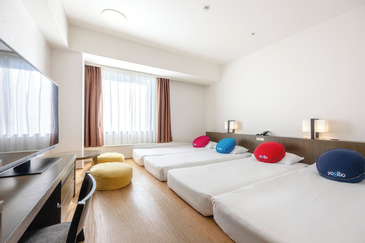 Une chambre d’hôtel avec deux lits, une télévision, un bureau et une fenêtre avec des rideaux.