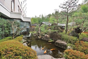 A koi pond surrounded by rocks and greenery, with a building in the background.