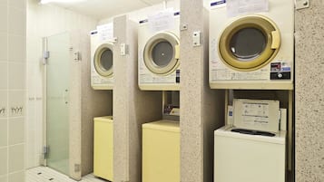A row of washing machines in a public laundry area with a tiled floor and a glass door entrance.