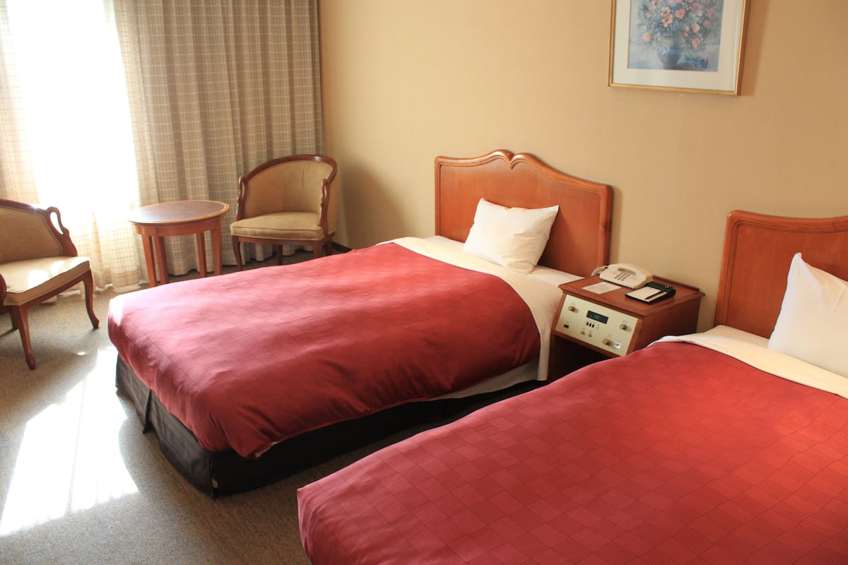 A hotel room with two beds, a chair, a small table, and a nightstand with a phone.