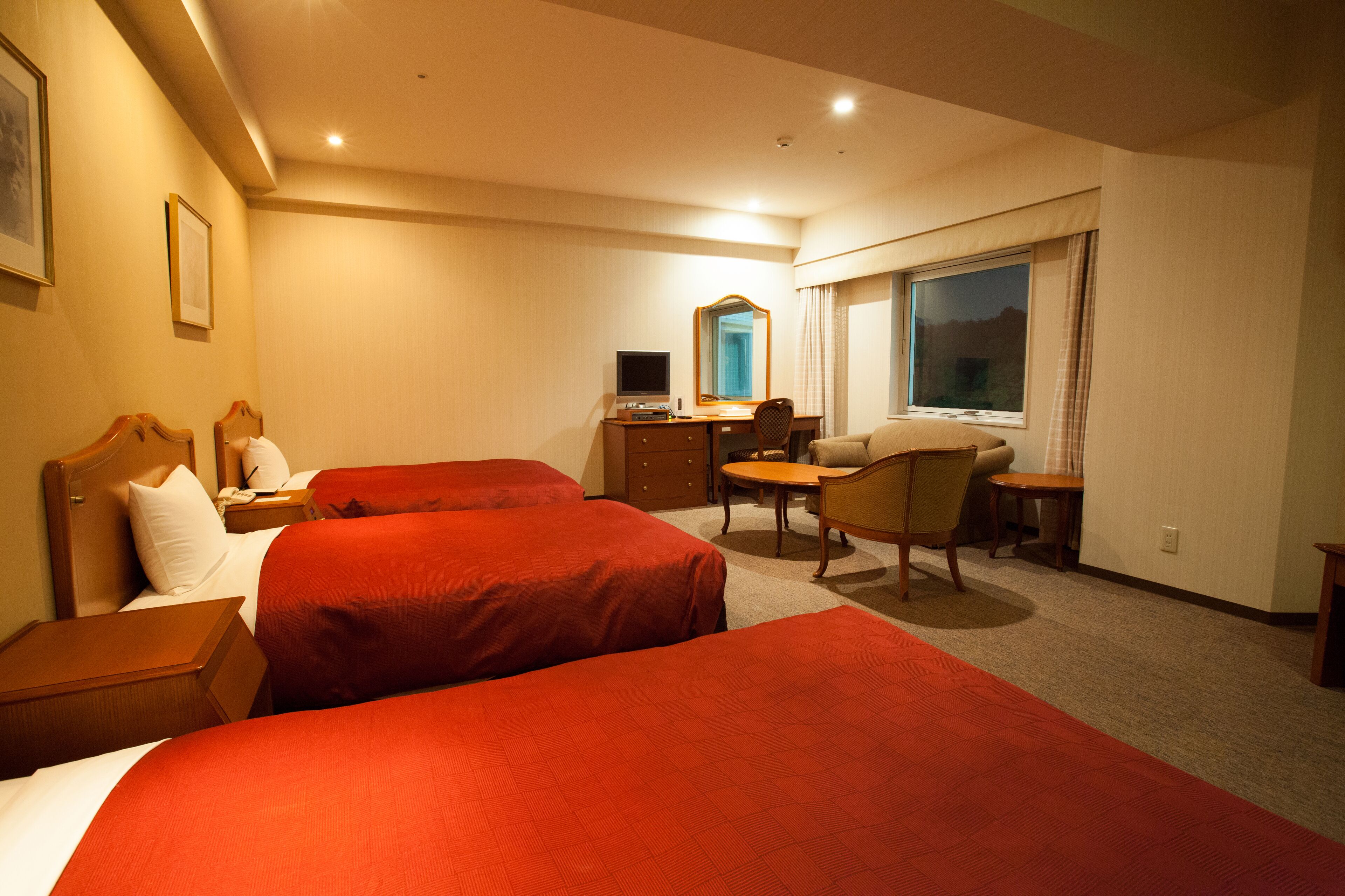 Une chambre d’hôtel avec deux lits, un bureau, une chaise, une petite table, un miroir et une fenêtre avec des rideaux.