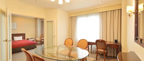 Habitación de hotel con una mesa de vidrio, cuatro sillas, un escritorio, una cama, un espejo y una araña.