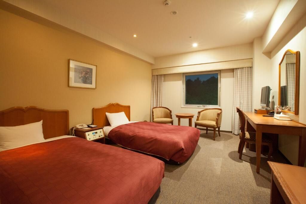 A hotel room with two beds, a desk, a chair, a small table, and a window with a view.