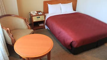 A hotel room with a bed, a wooden nightstand with a telephone, a chair, and a small table.