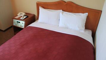 Habitación de hotel con cabecera de madera, colcha de edredón rojo, almohada blanca y mesita de noche con teléfono y bloc de notas.