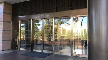 Entrada del The Gateway Hotel con puertas de cristal y estructura metálica, suelo de baldosas y un pilar de metal a la derecha.