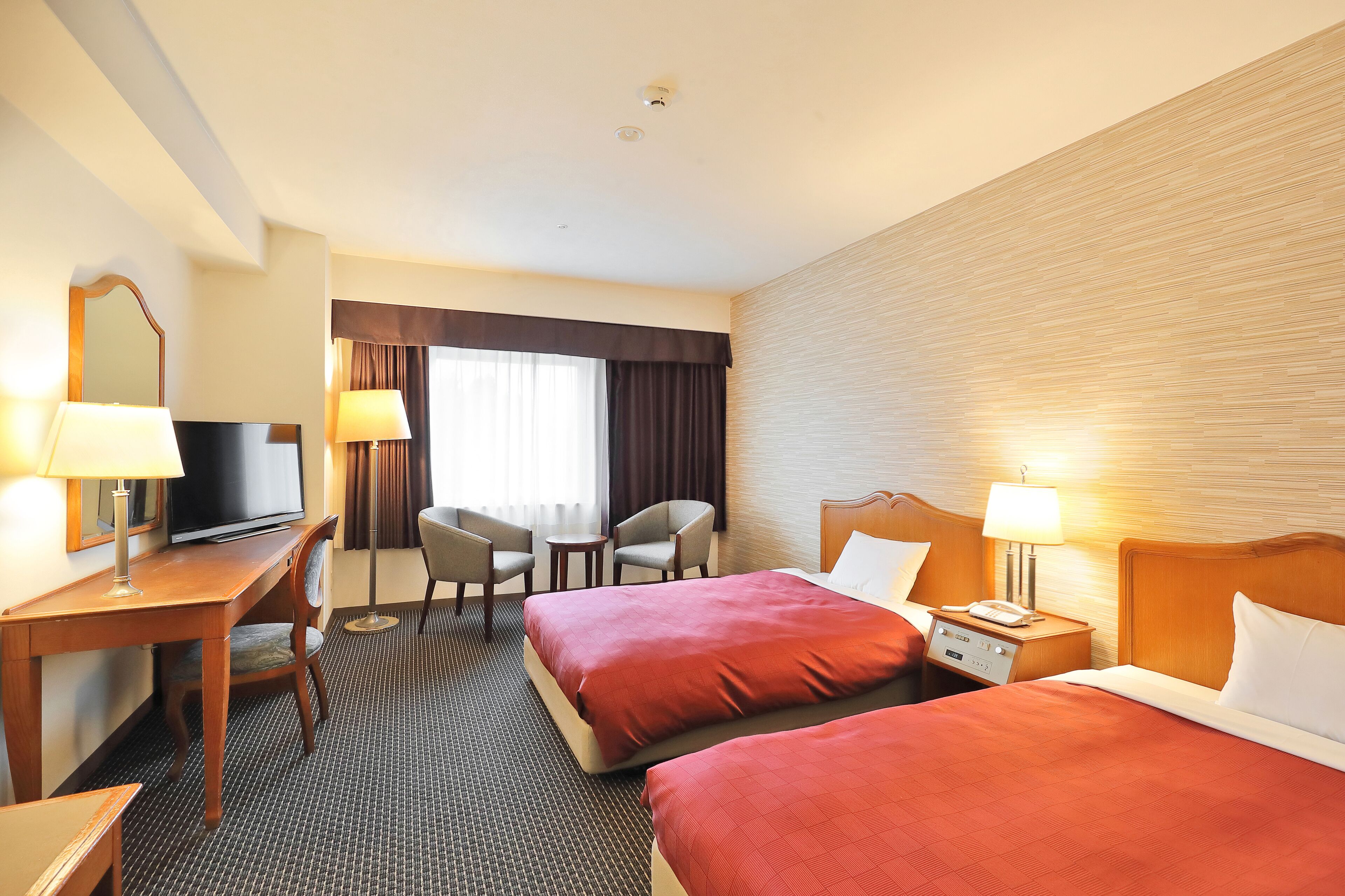 Une chambre d’hôtel avec deux lits, un bureau avec une télévision, une chaise et une petite table.