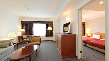 Habitación de hotel con sofá, una mesita, escritorio con lámpara, televisor en mueble bajo y cama con ropa de cama roja.
