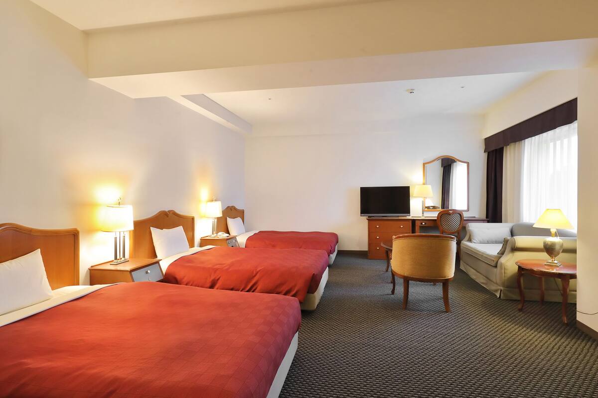 A hotel room with two beds, a TV, a desk, a chair, and a sofa.