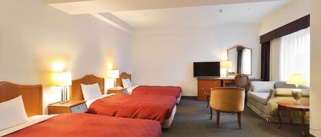 A hotel room with two beds, a TV, a desk, a chair, and a sofa.