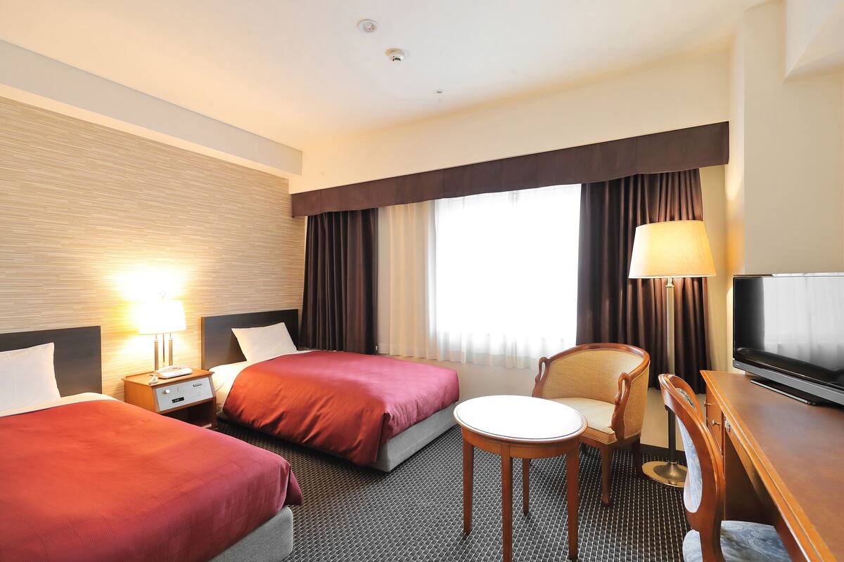 A hotel room with two beds, a desk with a chair, a television, and a lamp.