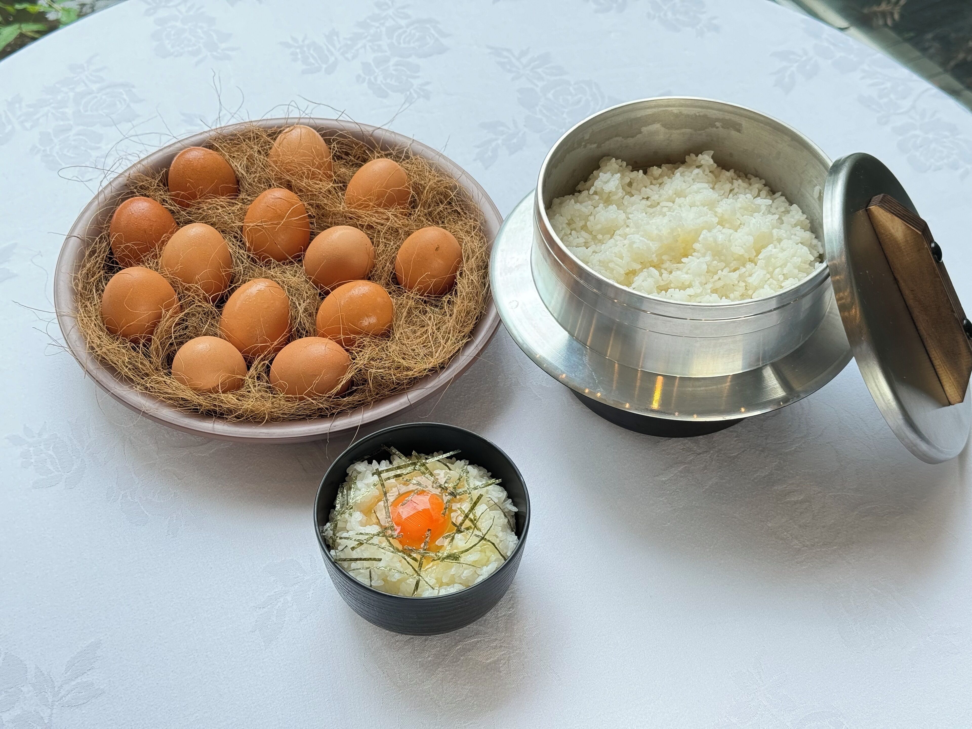 A table with a bowl of rice, a small bowl with an egg, and a bowl of eggs in a nest.