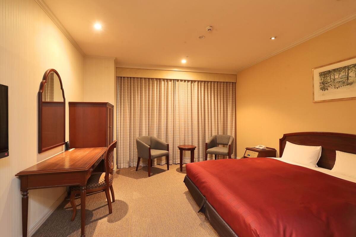 A hotel room with a large bed, two armchairs, a desk, a small table, and a mirror.