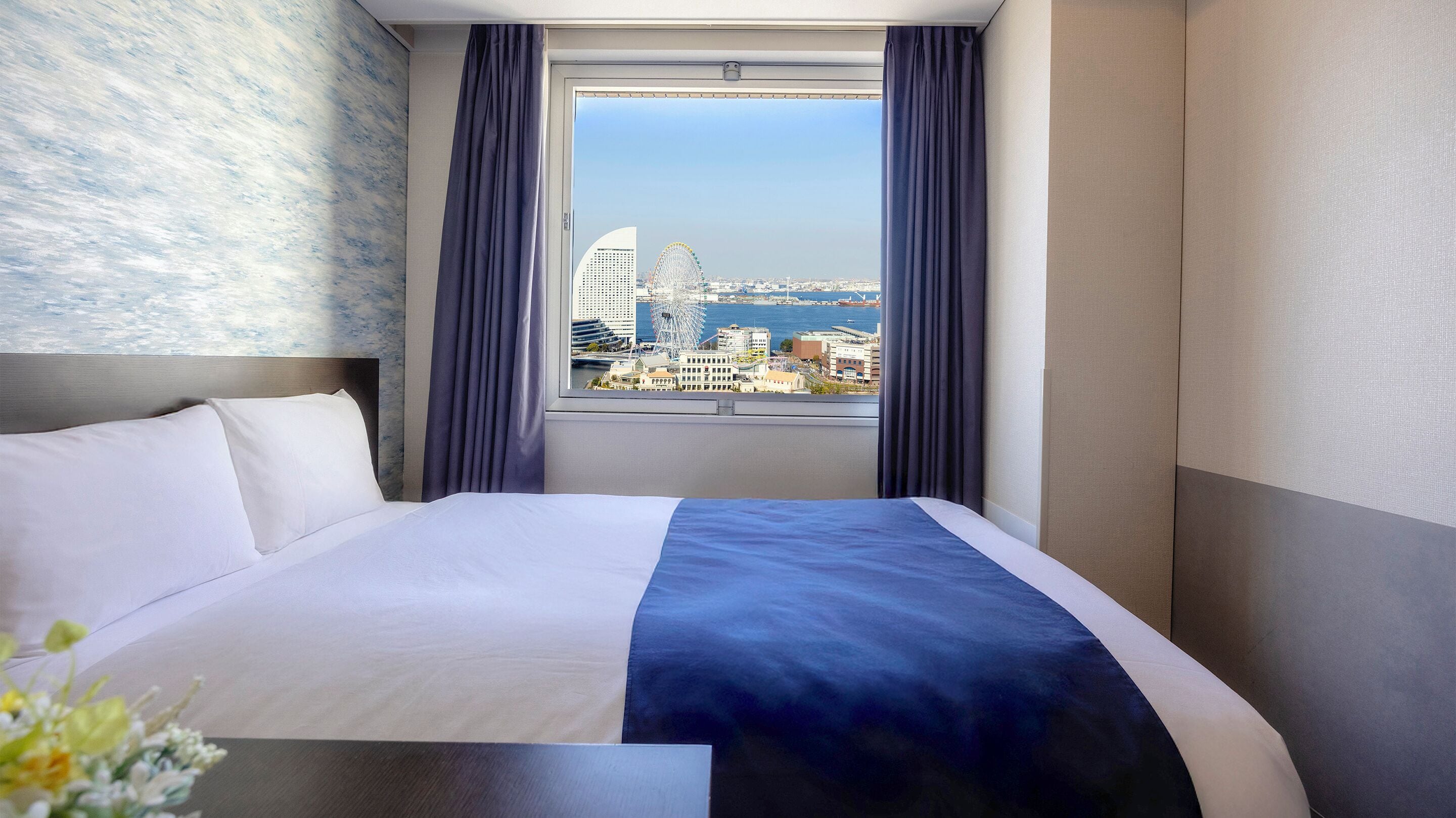 A hotel room with a large bed, a view of a cityscape, and a window with curtains.