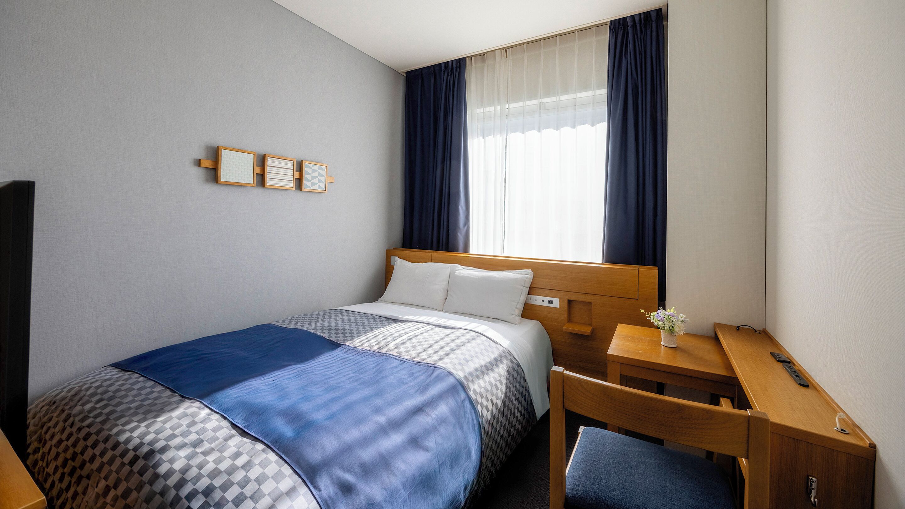 A hotel room with a bed, a desk, a chair, a TV, and a window with curtains.