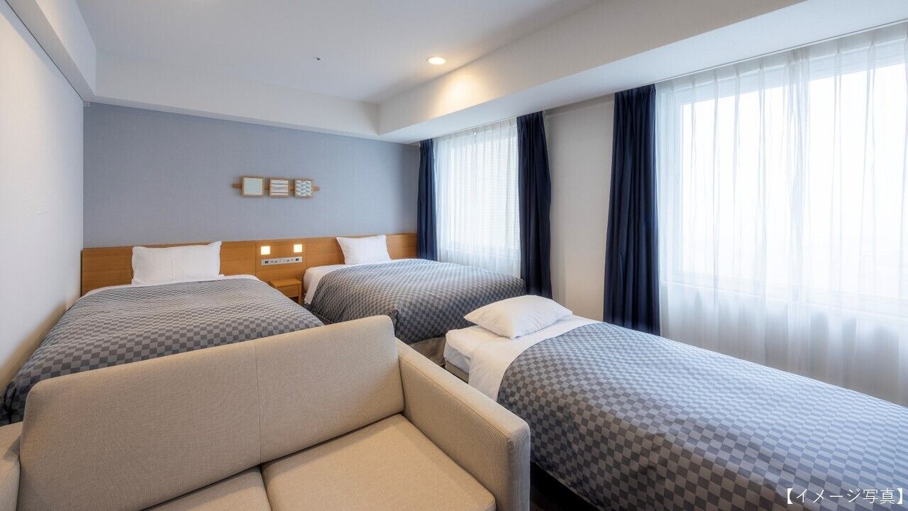 A hotel room with two single beds, a sofa, and a nightstand with a lamp.
