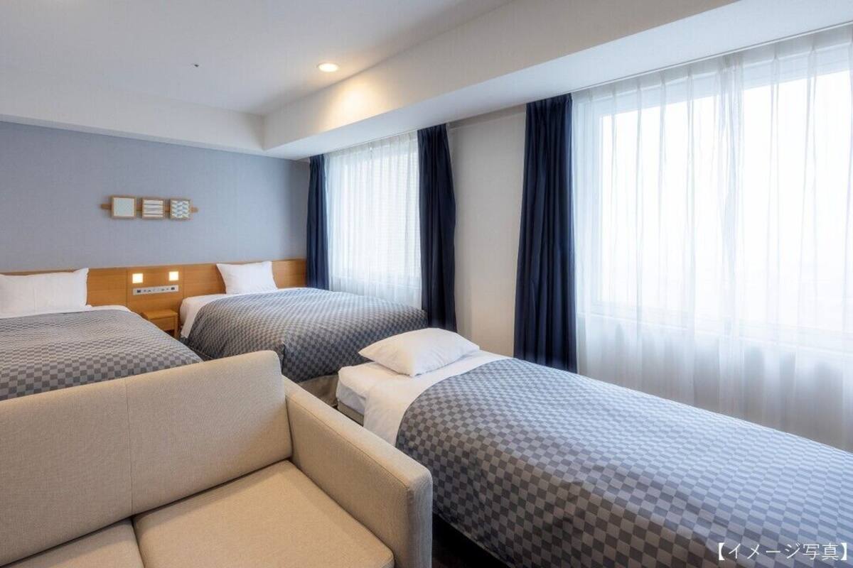 A hotel room with two single beds, a sofa, and a nightstand with a lamp.