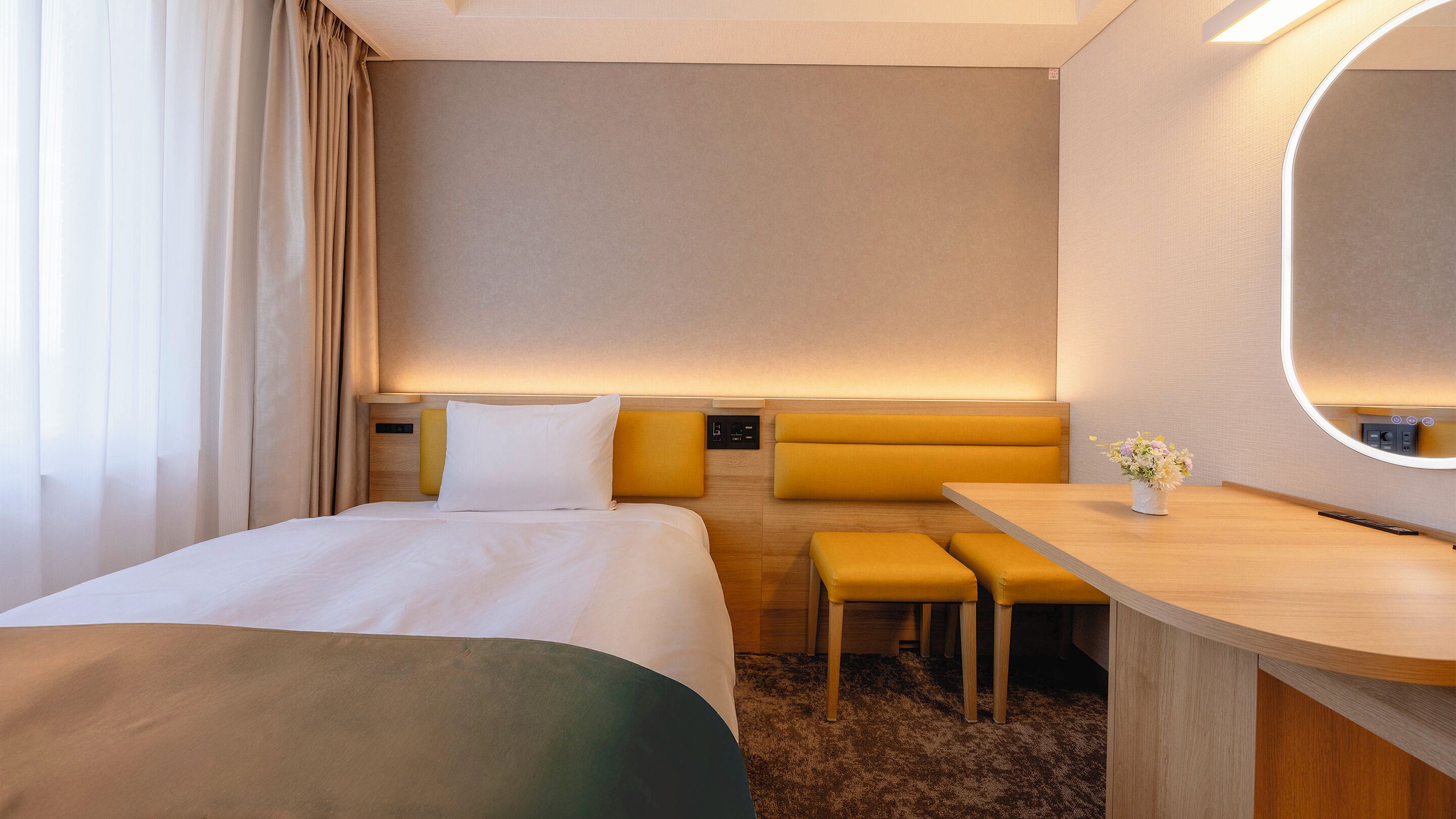 A hotel room with a bed, a desk, a bench, and a mirror.