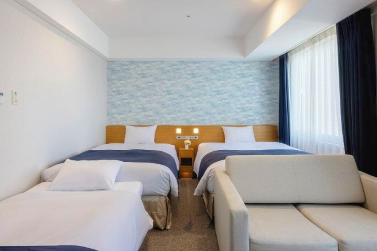 Ett hotellrum med två sängar, en soffa, ett sängbord med en lampa och utsikt över havet genom fönstret.