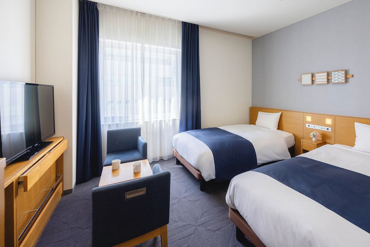 A hotel room with two beds, a TV, a desk, and a chair.