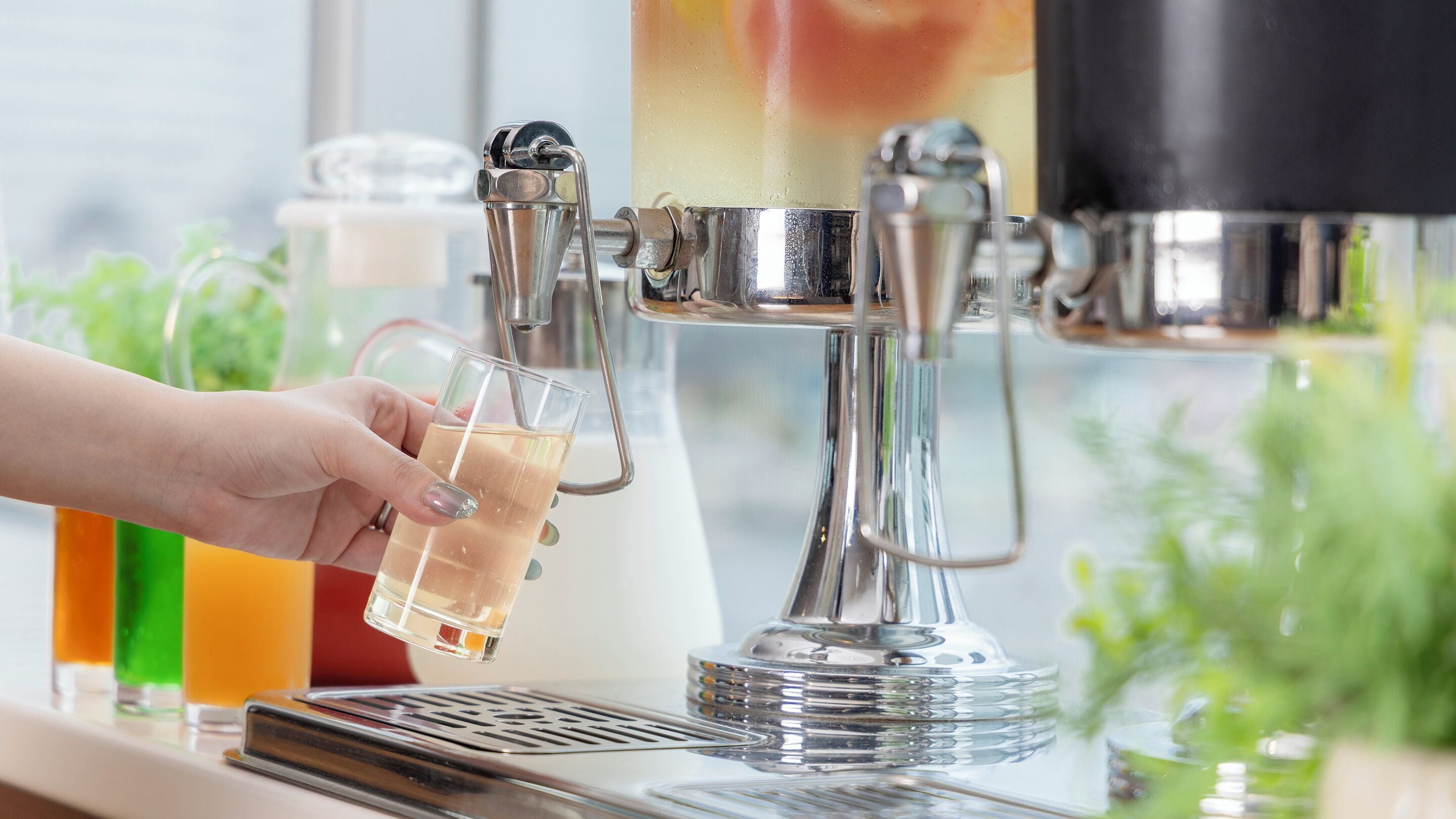 A hand holding a glass near a beverage dispenser.