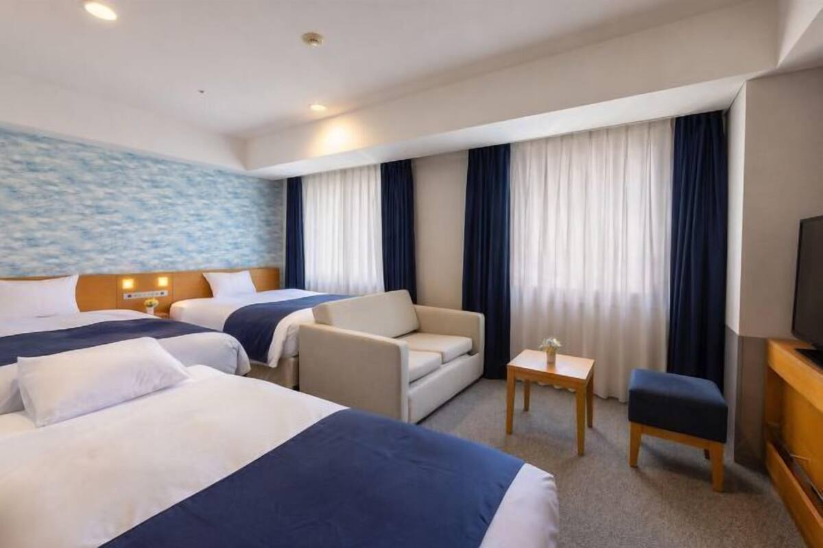 A hotel room with two beds, a sofa, a TV, and a small table.