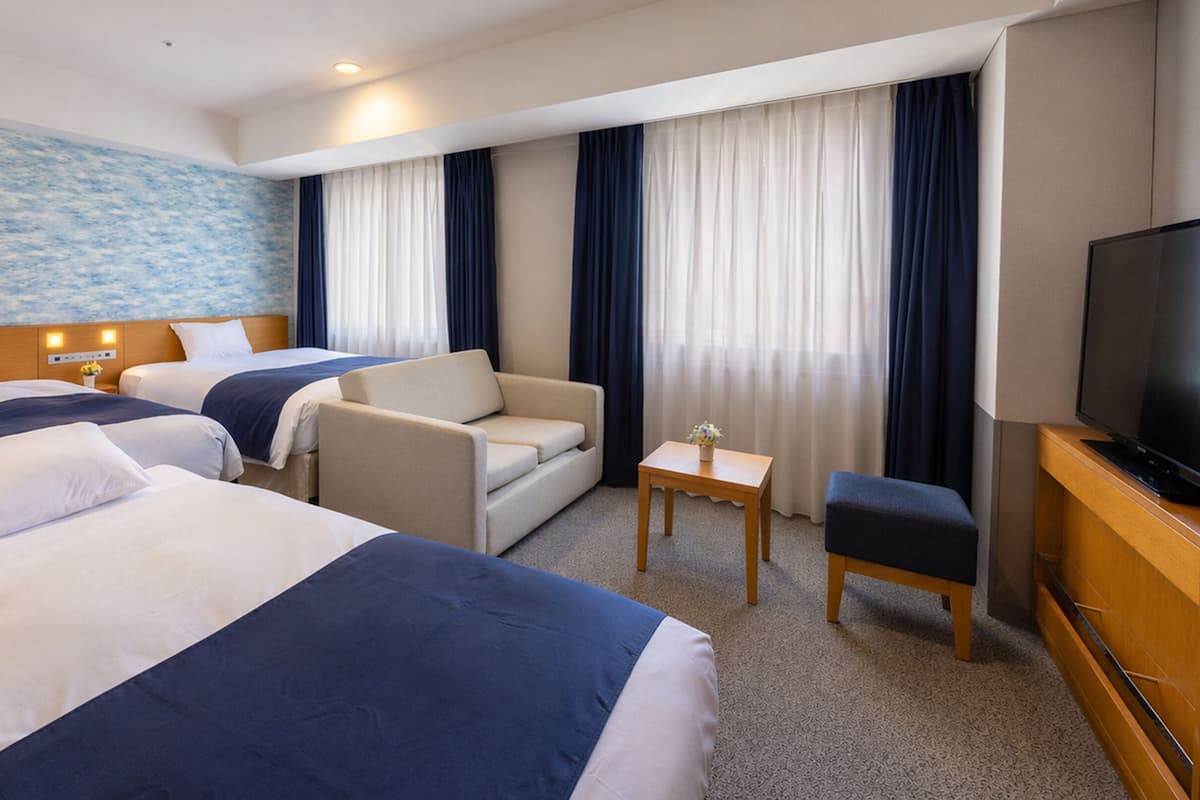 A hotel room with two beds, a sofa, a TV, and a small table.