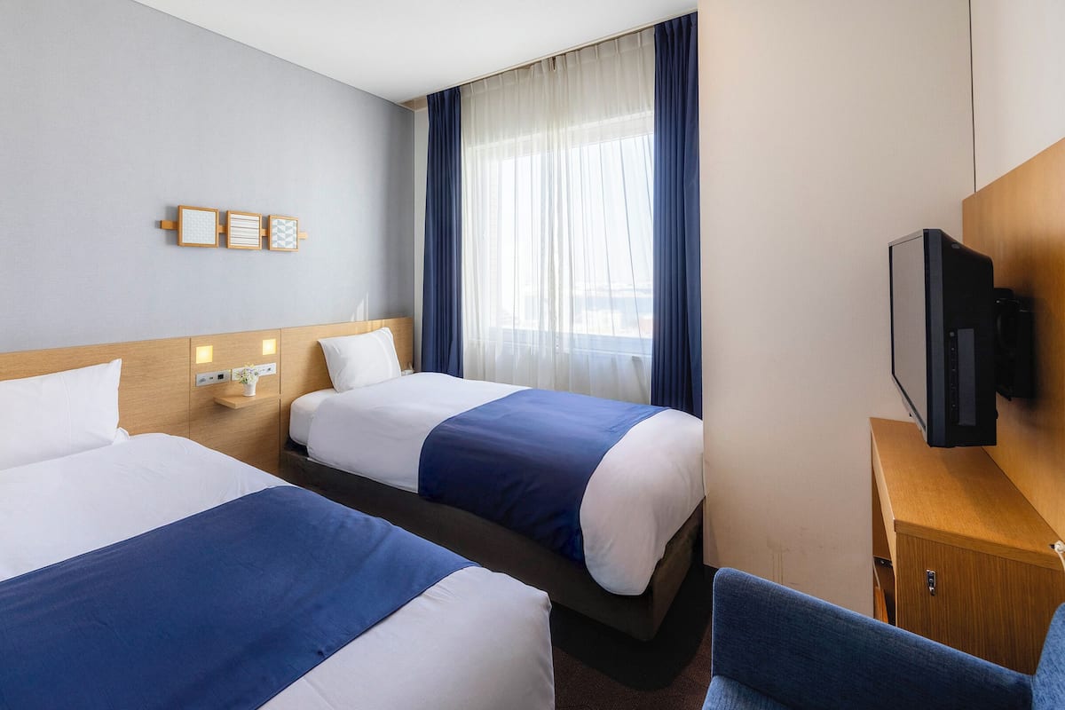 A hotel room with two beds, a television, a desk, and a window with curtains.