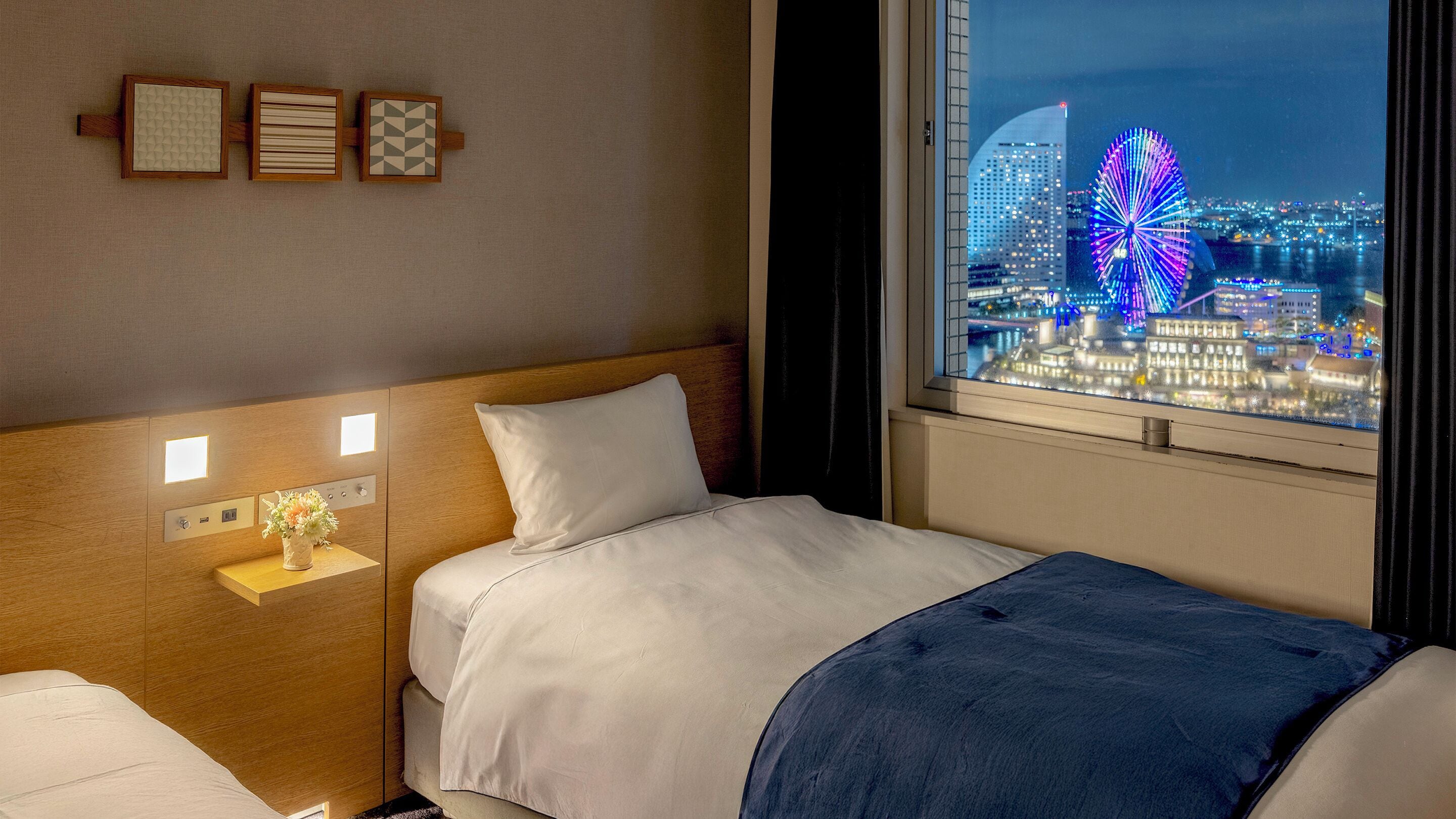 Una habitación de hotel con cama, mesita de noche y ventana con vistas a la ciudad.