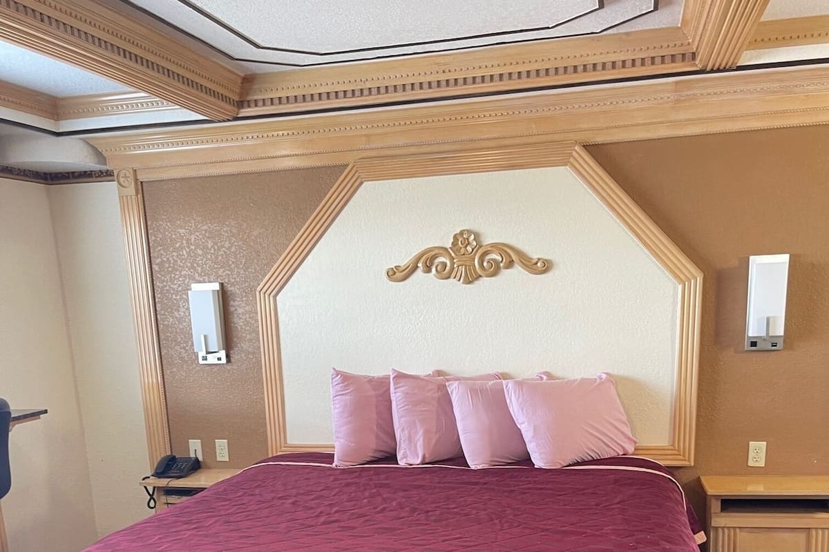 A hotel room with a large bed, a headboard with decorative elements, a bedside table, and a wall-mounted air conditioning unit.