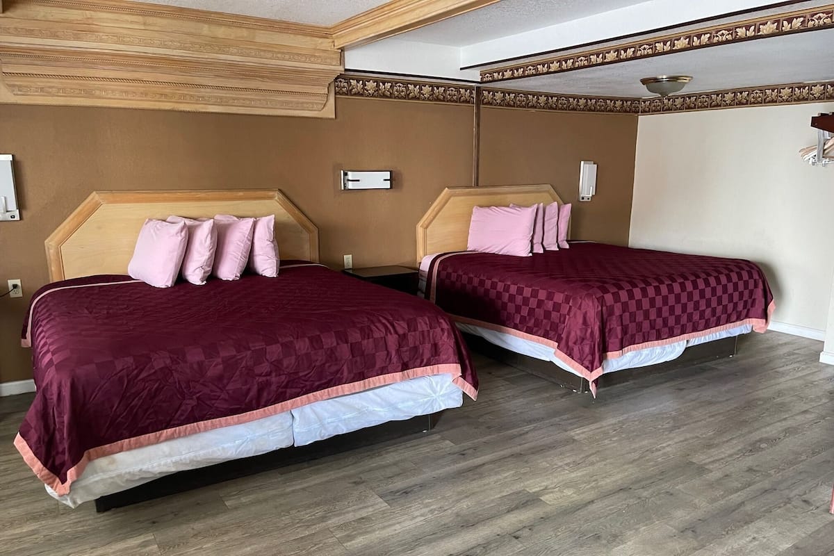 A hotel room with two beds, wooden headboards, and a wooden floor.