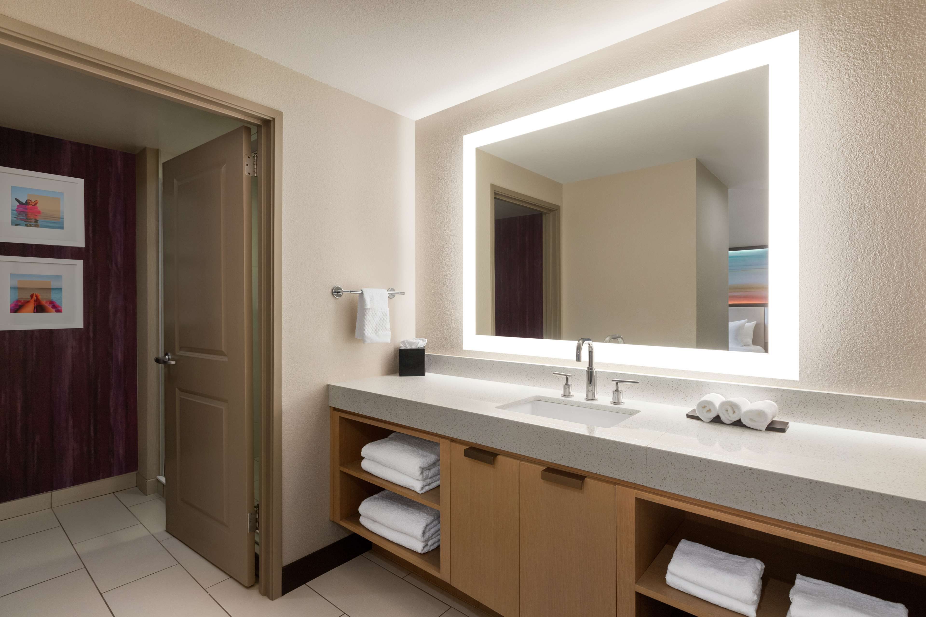 A modern bathroom with a large mirror, a sink, and wooden cabinets.