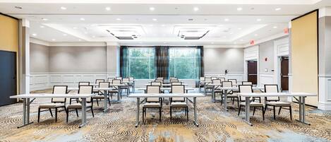 Una sala de conferencias con alfombra estampada, mesas y sillas blancas dispuestas para reuniones.