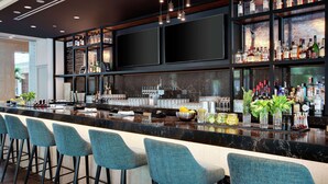 A bar area with a marble countertop, bar stools, shelves with liquor bottles, and a large flat-screen TV. - Embassy Suites by Hilton Tampa Downtown Convention Center (Tampa)